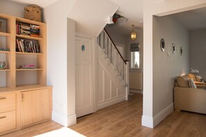 A hallway with a wooden bookshelf, a staircase, and a seating area with a sofa. - Hen Gi Mor: Pet-friendly home in Rhosneigr for 10 (Rhosneigr)