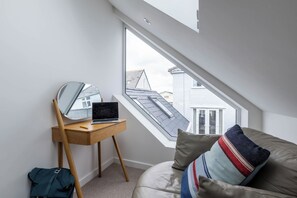 A bedroom with a skylight, a desk with a laptop, a mirror, and a sofa with cushions. - Hen Gi Mor: Pet-friendly home in Rhosneigr for 10 (Rhosneigr)