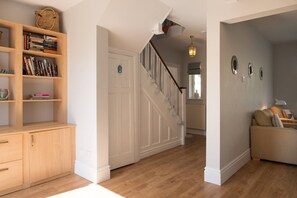 A hallway with a wooden bookshelf, a staircase, and a seating area with a sofa. - Hen Gi Mor : Spacious 4‑Bed Home with 3 Reception Rooms in Rhosneigr | Managed by Anglesey Holiday L (Rhosneigr)