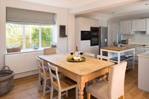 A modern kitchen with white cabinetry, a wooden dining table, and a view of greenery outside.