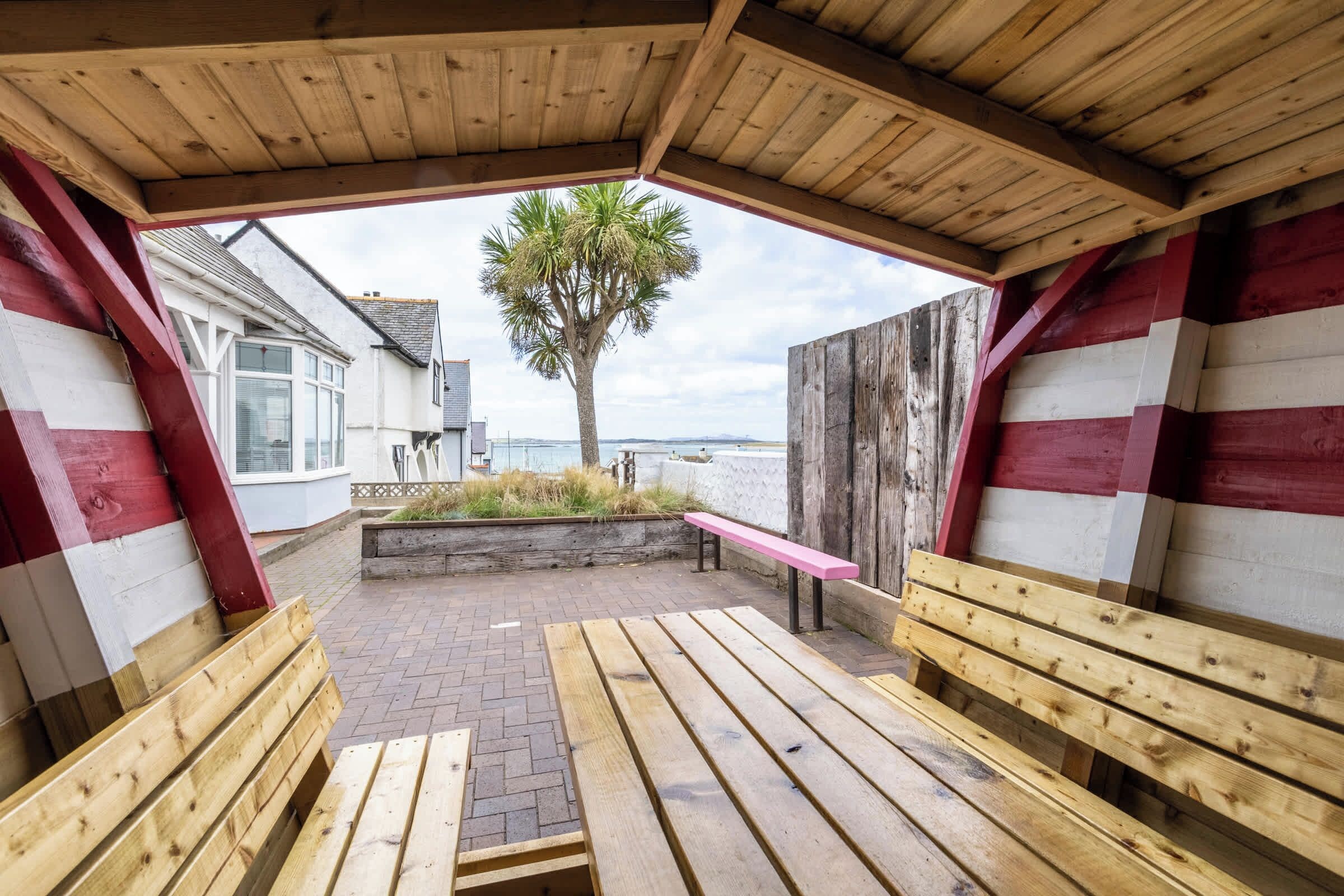 A wooden deck with benches, a palm tree, and a view of the sea.