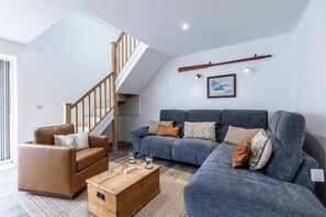 Un saló modern amb una escala, un sofà gris, un butàc armchair de cuir marró i una taula baixa de fusta.