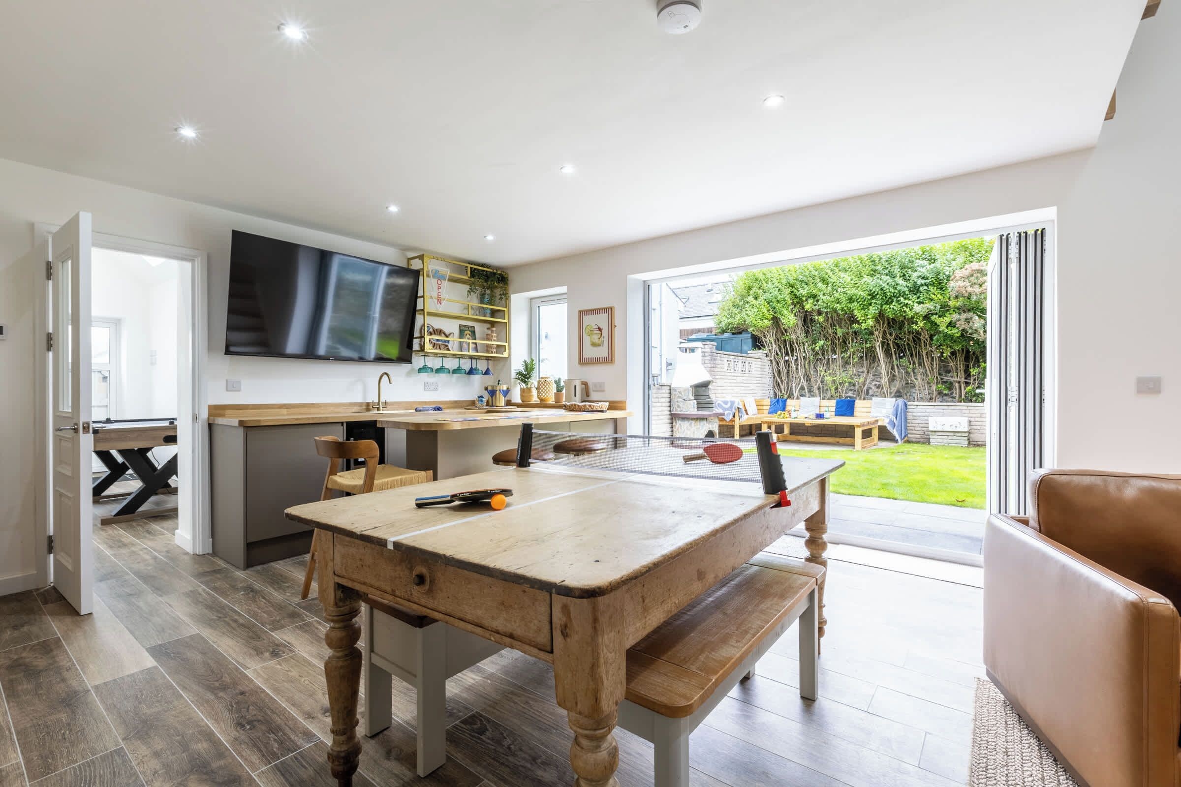 A modern kitchen with a dining area, a TV, and a view of a garden.