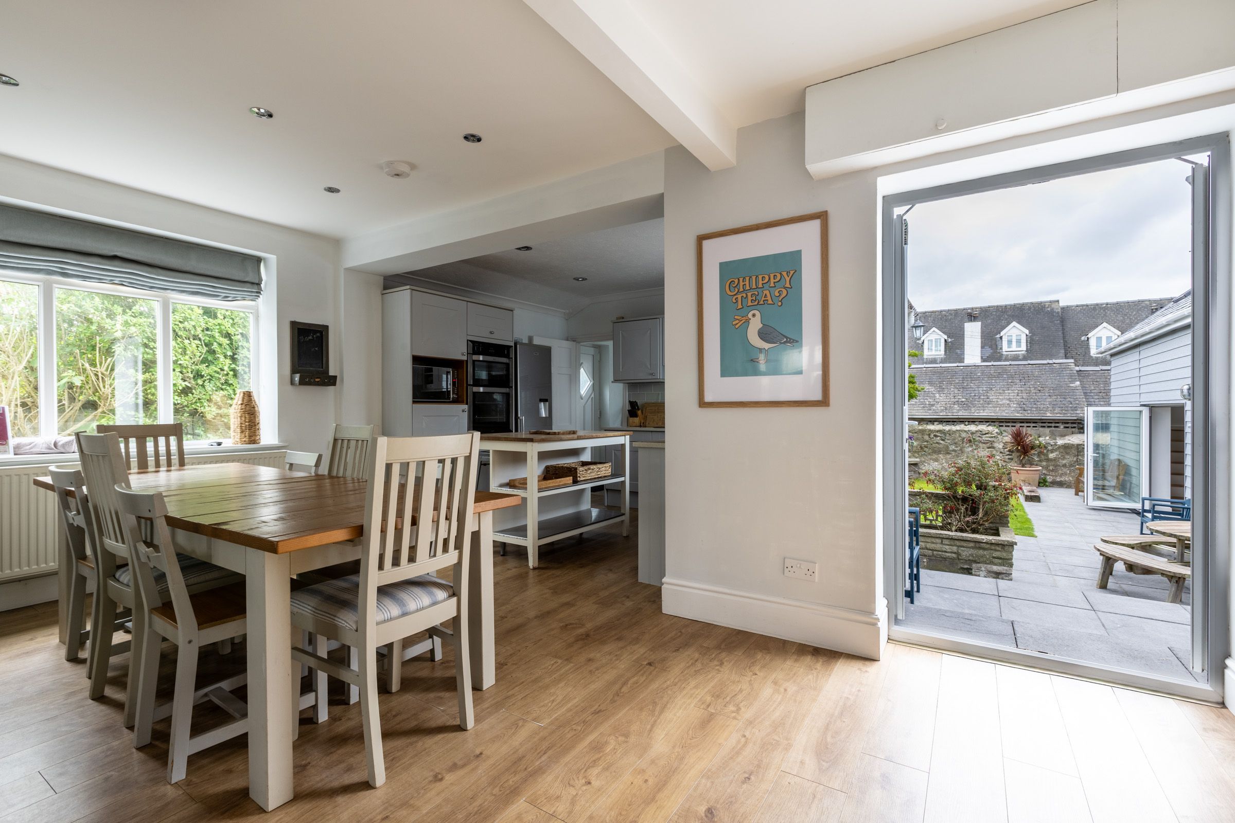 A spacious kitchen with modern appliances, a dining area with wooden furniture, and a view of the garden through a glass door.