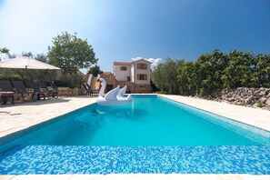 A swimming pool with a swan float, lounge chairs, and a stone building in the background. - Villa Nadia with private pool and grill (Dobrinj)