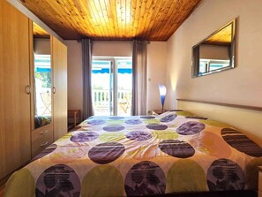 Un dormitorio con techo de madera, cama con colcha estampada, espejo en la pared y puerta corrediza de vidrio que da a un espacio exterior.