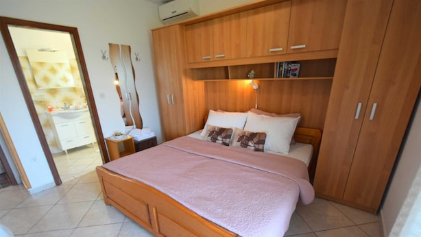 Ein Schlafzimmer mit einem hölzernen Bett, einem Nachttisch, einem Kleiderschrank und einem durch eine offene Tür einsehbaren Badezimmer.