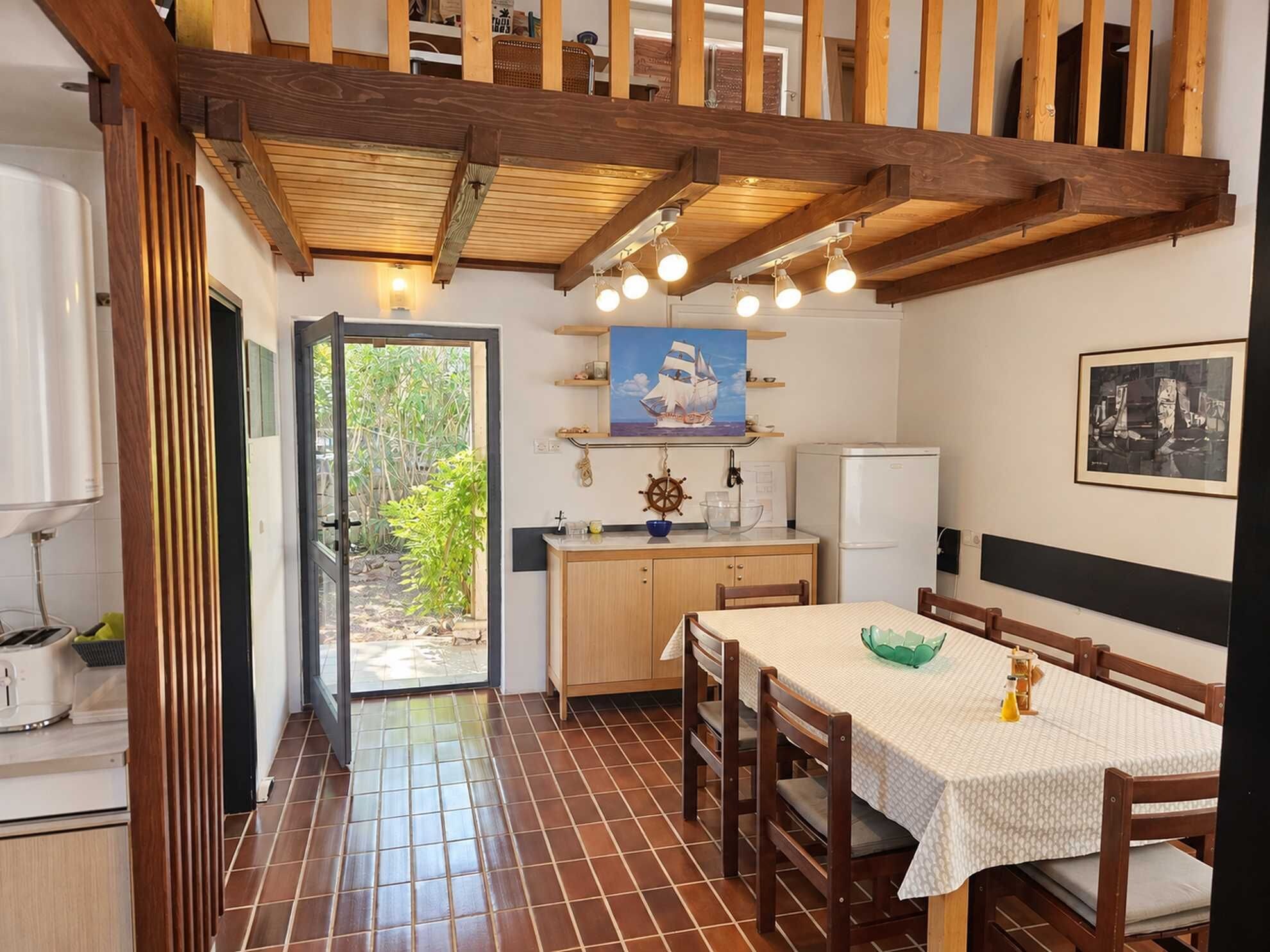 A compact kitchen with a dining area, wooden beams, and a view through the door.