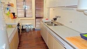 Une cuisine compacte avec des meubles blancs, un pare-feu en carrelage, un évier et un plan de travail muni d’une planche à découper.