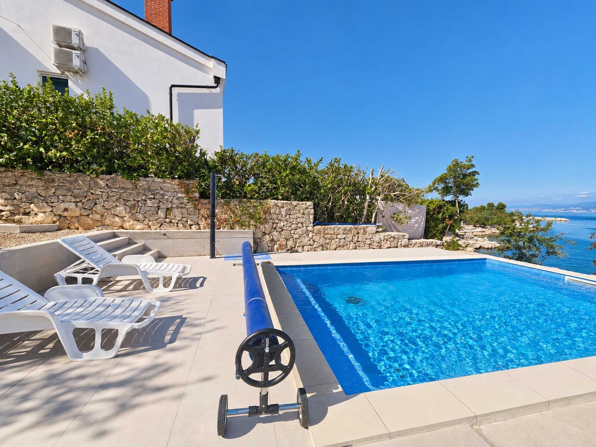 A swimming pool with lounge chairs and a steering wheel, surrounded by a stone wall and vegetation.