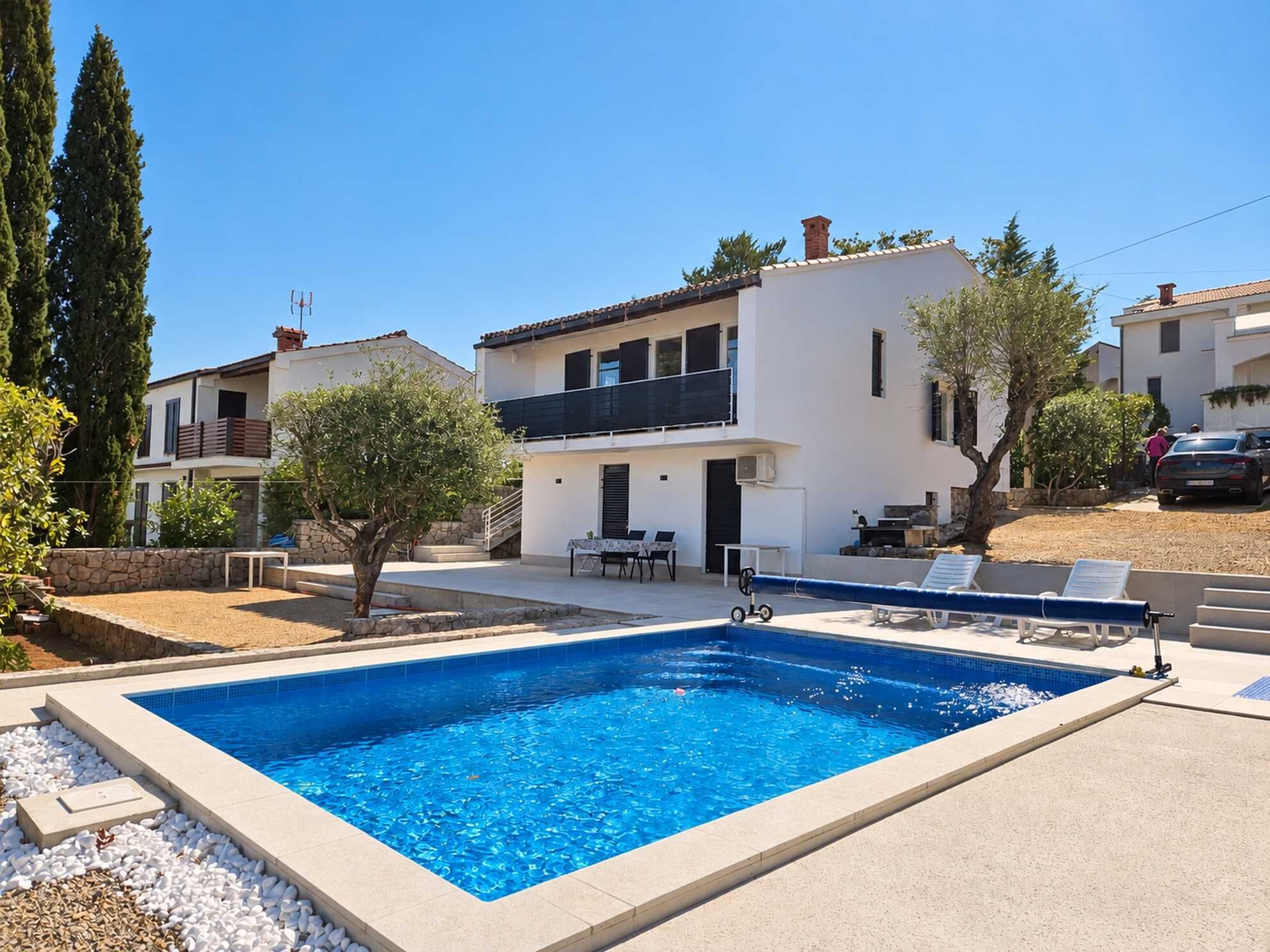 A residential property with a swimming pool, a patio with lounge chairs, and a stone wall.