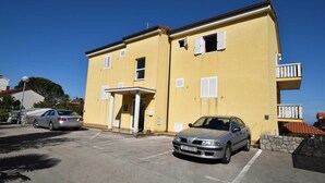 Un bâtiment jaune avec une entrée couverte, une voiture garée devant et un ciel bleu dégagé.