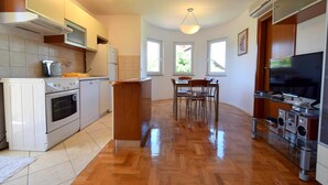 Une cuisine moderne équipée d’une cuisinière, d’un four et d’un four à micro-ondes, un coin repas avec une table et des chaises, et un téléviseur posé sur un meuble.