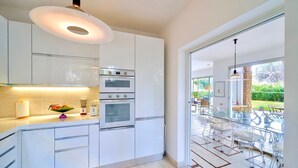 Une cuisine moderne avec des meubles blancs, un four encastré et un coin repas vitré offrant une vue sur le jardin.