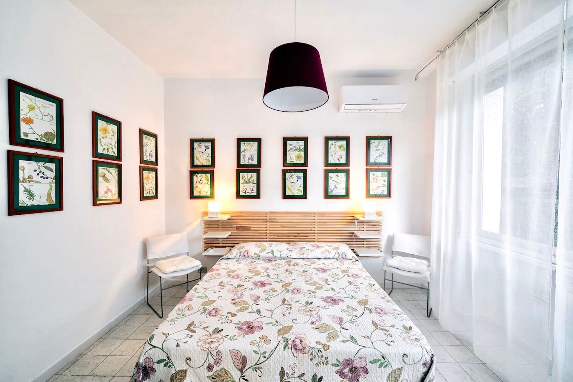 Un dormitorio con cama, escritorio, sillas e impresiones enmarcadas de plantas.