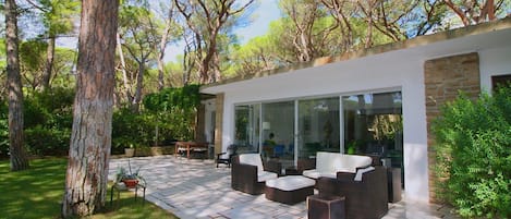 A modern outdoor patio with wicker furniture, a glass-enclosed dining area, and a stone wall.