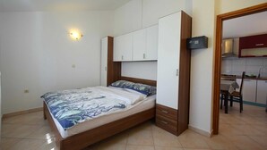 A compact bedroom with a bed, built-in wardrobe, and a kitchenette in the adjacent room.
