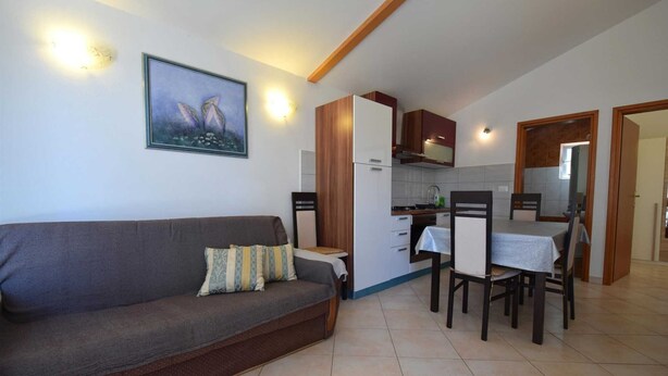 A living room with a sofa, a dining table with chairs, a kitchen area, and a framed picture on the wall.