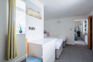 Une chambre d’hôtel avec un lit, un bureau et une chaise. Il y a une fenêtre avec des rideaux et une plante sur le rebord de la fenêtre.