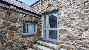 A stone building with a metal door and a window. - Ty Cwyfan: 3‑Bed Ground-Floor Apartment in Aberffraw | Managed by Anglesey Holiday Lettings (Ty Croes)