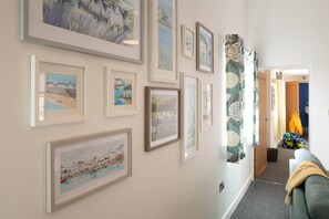 A hallway with framed artworks on the walls, a green sofa, and a door leading to another room.