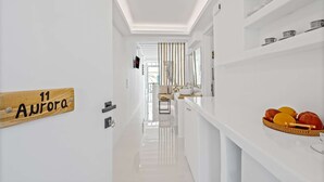 Un couloir d’hôtel moderne, avec une enseigne en bois indiquant « 11 Aurora », un élégant comptoir de réception blanc et un panier de fruits posé sur le comptoir.