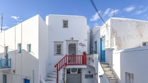 Une rue étroite bordée de bâtiments blancs, de portes bleues et d’un escalier rouge menant à un balcon.