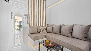 Un salon moderne avec un canapé d’angle beige, une table basse en verre avec un plateau et un séparateur de pièce en lattes de bois.