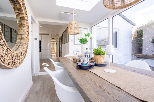 Enjoy meals in this dining area with a long table, white chairs, and a wicker light fixture.