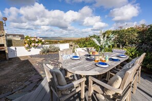 An outdoor dining area with a round wooden table set for four, surrounded by cushioned chairs. - Hafan: Pet-friendly beach-front holiday cottage in Rhosneigr (Rhosneigr)