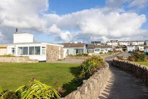 A row of residential buildings with a grassy area in the foreground and a paved path leading to the buildings. - Hafan: Pet-friendly beach-front holiday cottage in Rhosneigr (Rhosneigr)
