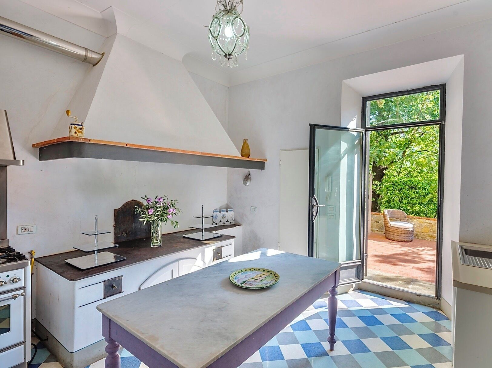 A kitchen with a central island, a built-in oven, a gas stove, a hanging light fixture, and a sliding glass door leading to an outdoor area.
