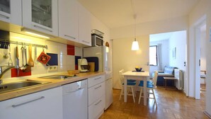Una cocina compacta con muebles blancos, lavavajillas y un comedor con mesa y sillas.