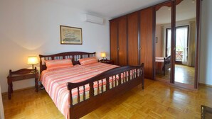 Un dormitorio con una cama de madera, dos mesitas de noche con lámparas, un armario grande y un cuadro enmarcado en la pared.
