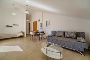 A modern living room with a sofa, a glass coffee table, a dining area with chairs, and pendant lighting.