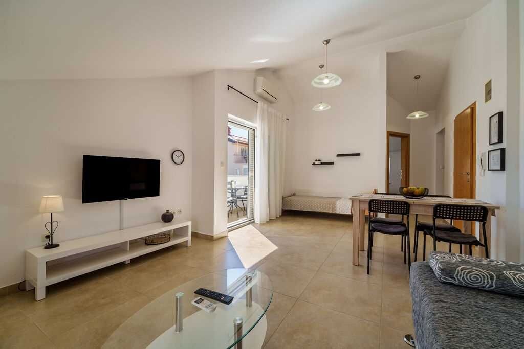 A modern living room with a flat-screen TV, a glass coffee table, a sofa, and a dining area with chairs and a table.