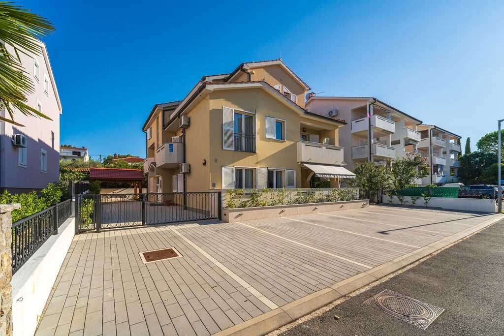 Un edificio residencial de varios pisos con balcones, un camino pavimentado y un cielo despejado.
