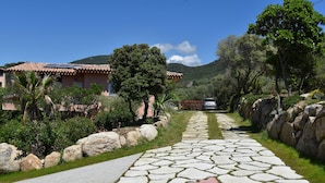 A paved pathway leading to a building with a tiled roof, surrounded by greenery and rocks. - Olmeto Plage: Large 3-bedroom apartment 200 metres from the sea (Olmeto)