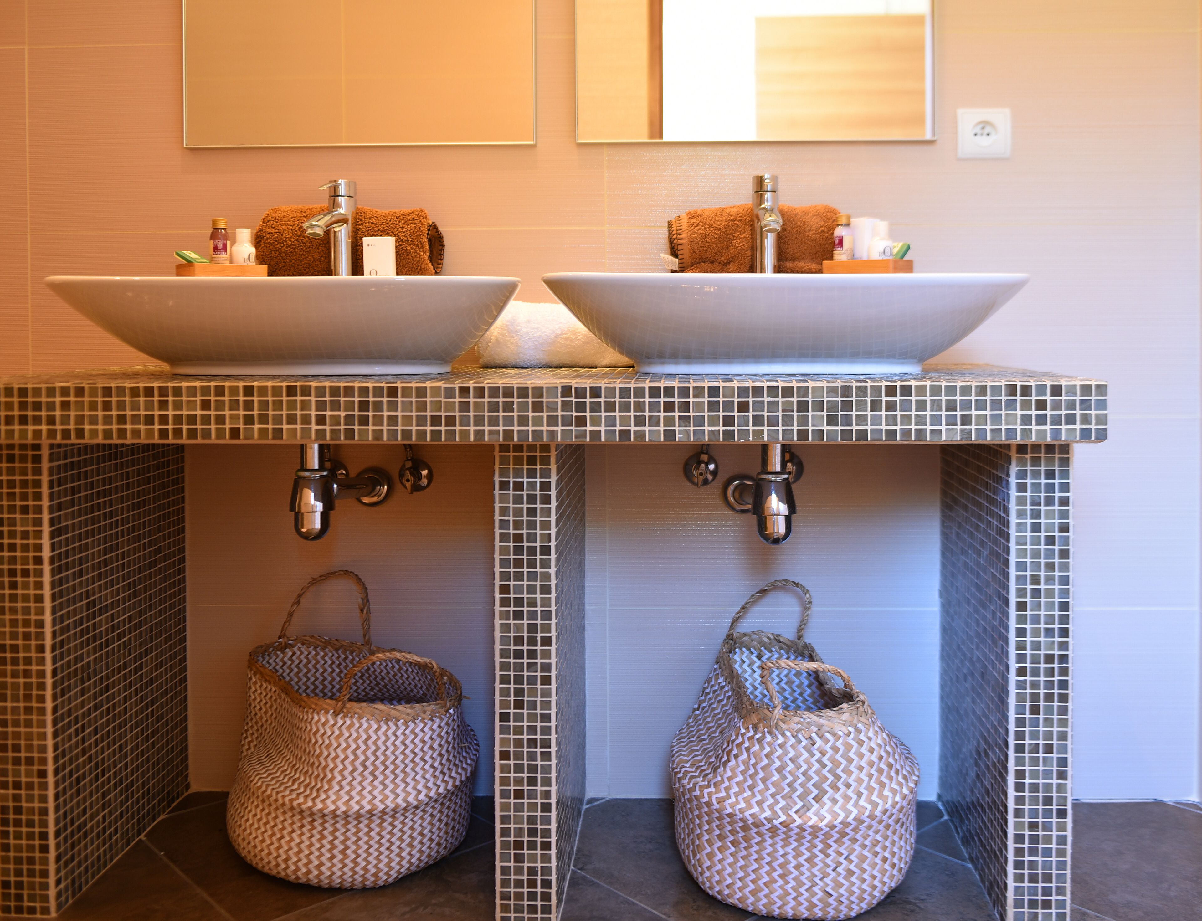 Une salle de bain avec deux lavabos, un miroir et deux paniers en osier placés sous les lavabos.