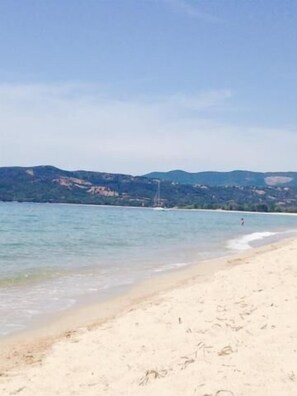 Uma praia com águas cristalinas, areal arenoso e colinas ao longe.