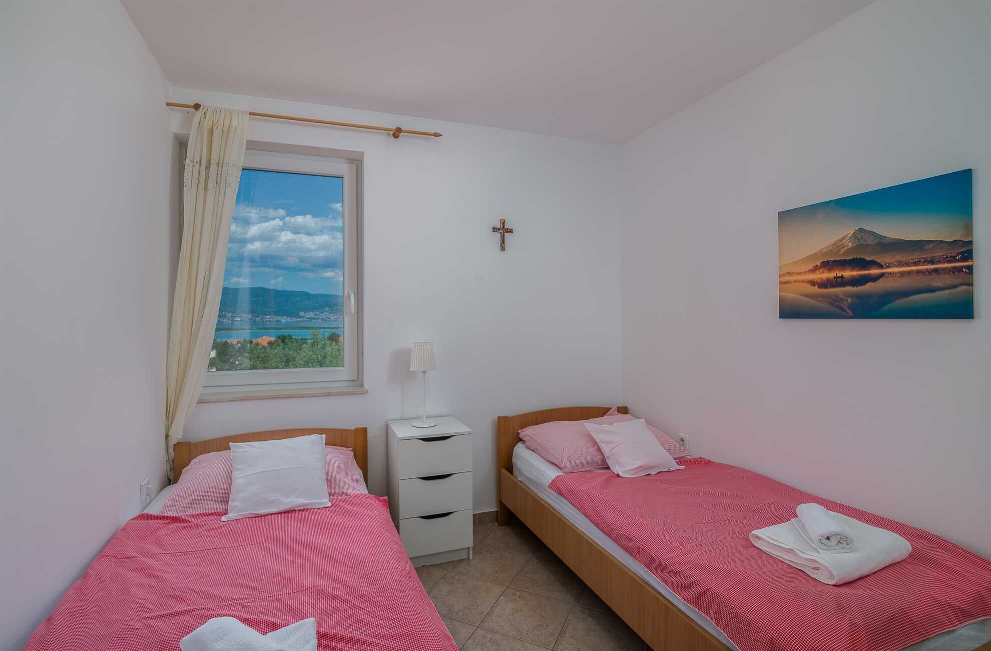 Een slaapkamer met twee bedden, een raam met uitzicht, een kruis aan de muur en een schilderij van een berg.