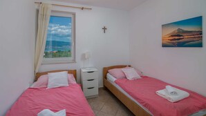 A bedroom with two beds, a window with a view, a cross on the wall, and a painting of a mountain. - Apartment Šop with balcony (Čižići)