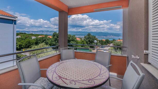A balcony with a round table and chairs, offering a view of a coastal landscape with mountains and a body of water. - Apartment Šop with balcony (Čižići)