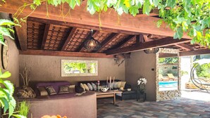 A cozy outdoor seating area with a wooden pergola, a cushioned bench, and a stone wall.