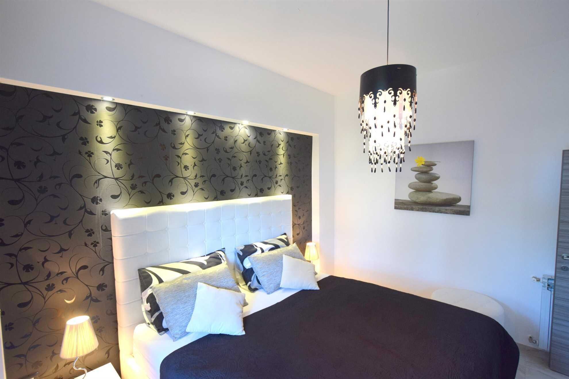 A bedroom with a large bed, a decorative headboard, a hanging light fixture, and a wall-mounted artwork.