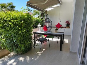 Un patio con mesa y sillas, rodeado de follaje y una silla colgante.