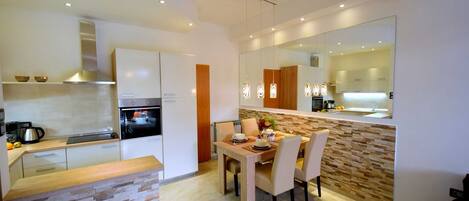A modern kitchen with a dining area, featuring a stone countertop, a built-in oven, and a large mirror above the counter.