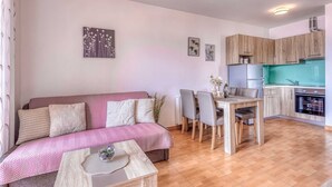 A cozy living room with a sofa, a coffee table, and a dining area with chairs and a table. There is a kitchen with wooden cabinets and a refrigerator. - Apartment Baran with a Sea View (Čižići)
