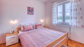 A bedroom with a bed, bedside tables, a window with curtains, and a wall-mounted light fixture. - Apartment Baran with a Sea View (Čižići)