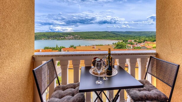A balcony with a table and chairs, overlooking a lake and a town. - Apartment Baran with a Sea View (Čižići)